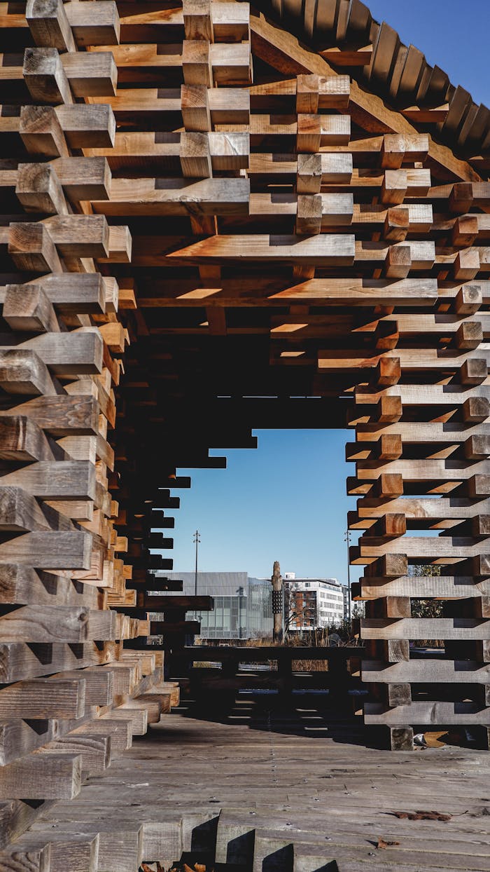 A geometric wooden installation frames a distant cityscape beneath a clear blue sky.